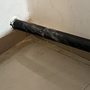 צינור שחור מחובר לקיר עם חומר איטום לבן