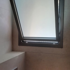 חלון ציר מאלומיניום כהה עם זכוכית חלבית בחדר רחצה