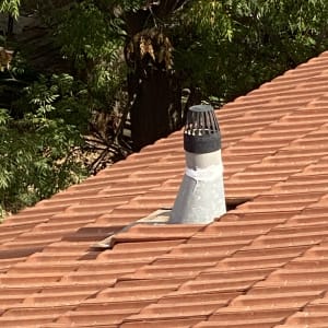 ארובה על גג רעפים אדומים עם צמחייה ברקע