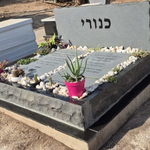 מצבה עם כיתוב בעברית וצמחים מסביב