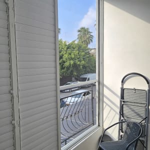 חלון עם תריסים, כיסא מתקפל ושולחן קטן במרפסת