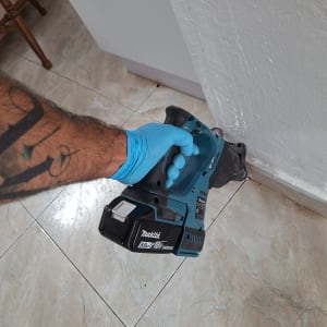 יד עם כפפה כחולה מחזיקה מקדחה חשמלית ליד קיר