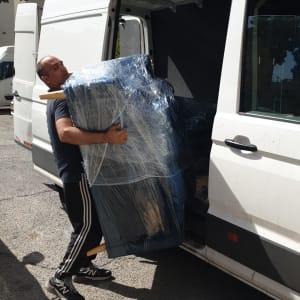 אדם מעמיס רהיט עטוף בניילון לרכב מסחרי לבן