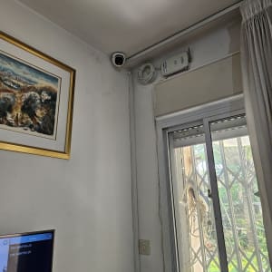 מצלמת אבטחה מותקנת בפינת החדר ליד חלון עם סורגים.