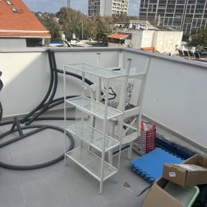 מדף מתכת לבן על מרפסת עם קופסאות וציוד אחר