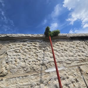 מטאטא עם ידית אדומה מנקה קיר אבן גבוה