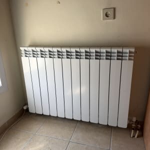 רדיאטור חימום לבן מותקן על קיר כחלק ממערכת הסקה ביתית