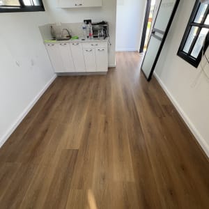 רצפת פרקט בחדר עם מטבחון קטן ודלת זכוכית.