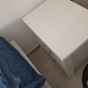 שידה לבנה ליד מיטה עם כרית כחולה