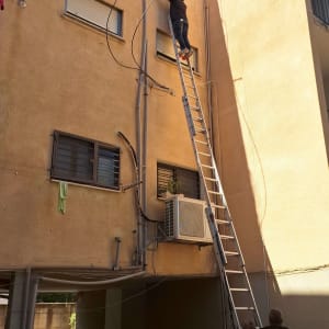 עבודת אינסטלציה ואיטום צנרת בגובה על קיר חיצוני של בניין מגורים
