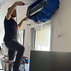 טכנאי מתקין מזגן עם כיסוי כחול על סולם