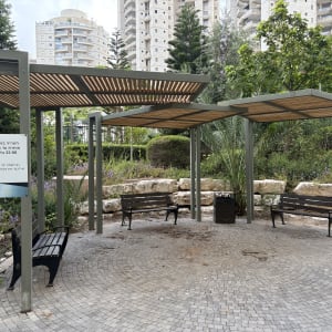 פרגולה עם ספסלים בגינה ציבורית ליד בניינים גבוהים