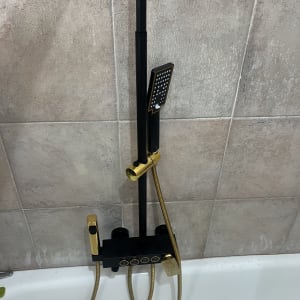 ברז מקלחת עם צינור זהב על קיר אריחים