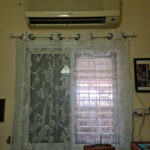 מזגן מותקן מעל חלון עם וילון תחרה