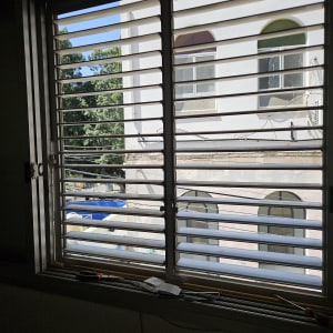 תריסים פתוחים עם נוף של בניין ועצים בחוץ