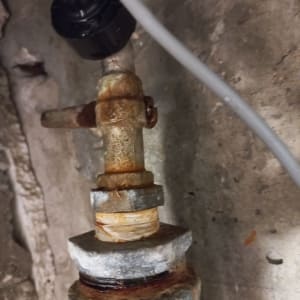 צינור חלוד עם חיבורים על קיר בטון