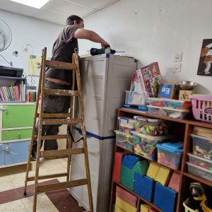 אדם על סולם עובד עם מקדחה בחדר מלא צעצועים