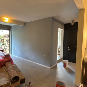 קיר צבוע באפור עם דלי צבע ומברשת על הרצפה