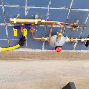 צנרת גז עם ברזים ומחברים על קיר אריחים כחול