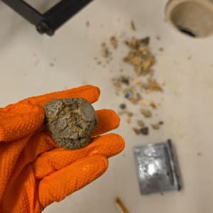 כפפה כתומה מחזיקה גוש חומר על רקע שולחן