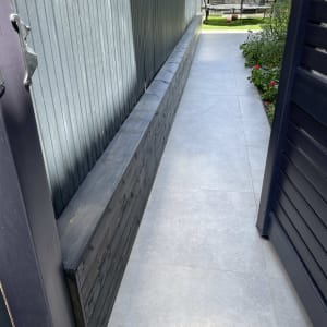 גדר עץ כהה לצד שביל מרוצף בגינה