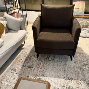 כורסה חומה על שטיח מעוצב בסלון עם מדף ספרים.