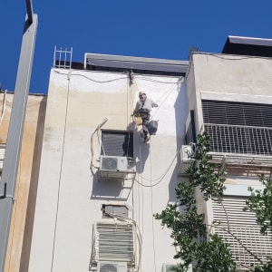 אדם על חבלים צובע קיר חיצוני של בניין