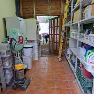 חדר שירות עם מדפים, מכונת כביסה, שואב אבק וסולם.