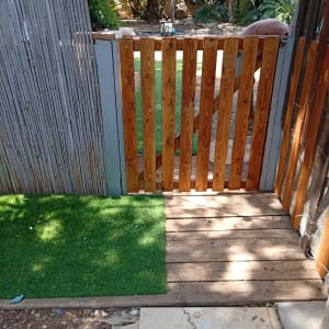 שער עץ עם דשא מלאכותי ועצים ברקע