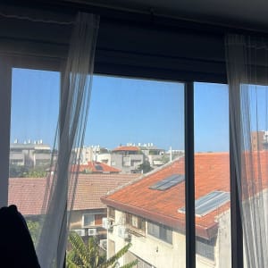 חלון עם וילונות ונוף של גגות בתים