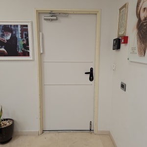 דלת לבנה עם ידית שחורה ומנגנון סגירה עליון