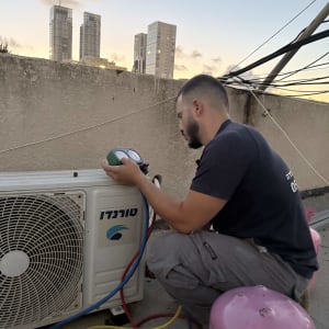 טכנאי בודק מזגן על גג עם בלוני גז