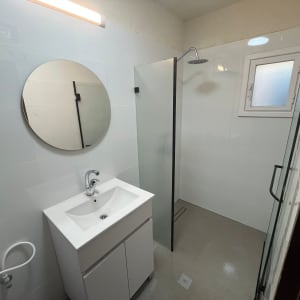 חדר אמבטיה משופץ עם מקלחון, כיור ומראה עגולה