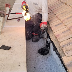 אדם עובד על גג עם מבער להלחמת זפת