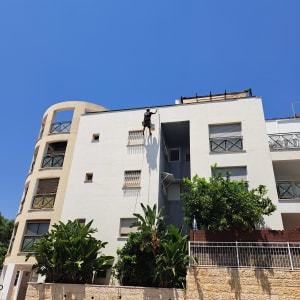 אדם תלוי על חבל צובע קיר חיצוני של בניין