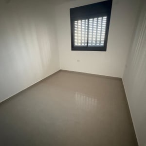 חדר ריק עם רצפת קרמיקה וחלון עם תריסים סגורים