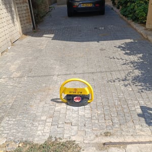 מחסום חניה צהוב על שביל מרוצף עם רכב ברקע