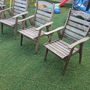 שלושה כיסאות עץ על דשא סינתטי בגינה