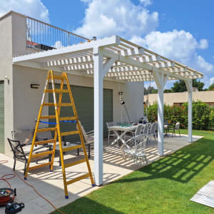 סולם צהוב ליד פרגולה לבנה בגינה