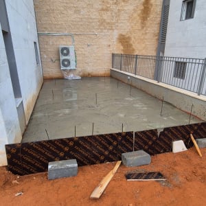 יציקת בטון חדשה ליד קיר חיצוני עם יחידת מיזוג אוויר