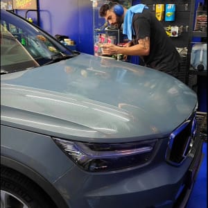 אדם מלטש מכסה מנוע של רכב עם מכונת ליטוש