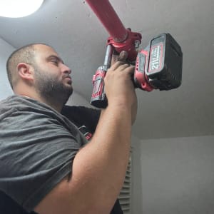 אדם מתקין צינור אדום בתקרה עם כלי עבודה