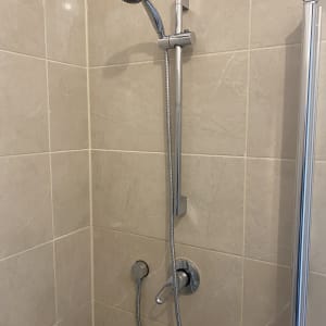 ראש מקלחת מתכוונן עם צינור מתכת על קיר אריחים