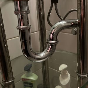 כיור עם צנרת מתכת ומוצרי טיפוח מתחתיו