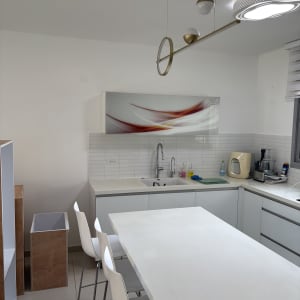 מטבח מודרני עם שולחן וכיסאות לבנים, כיור וברז, מכשירי חשמל על השיש