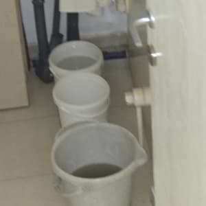 דליים לאיסוף מים על רצפה מרוצפת לצד צנרת