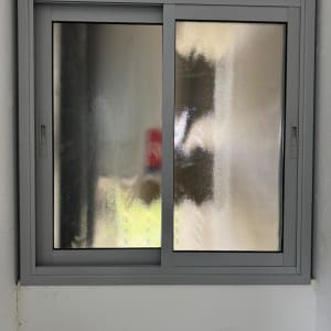 חלון זכוכית עם מסגרת אפורה על קיר לבן.