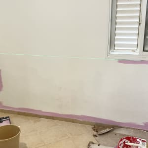 חדר עם קיר צבוע חלקית בצבע ורוד וכלי עבודה לצביעה