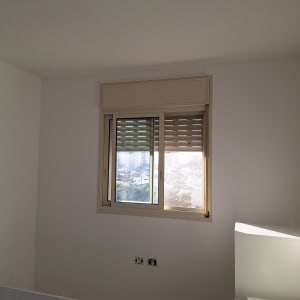 חדר צבוע בלבן עם חלון ותריסים