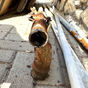 צינור חלוד על מדרכה ליד קיר אבן